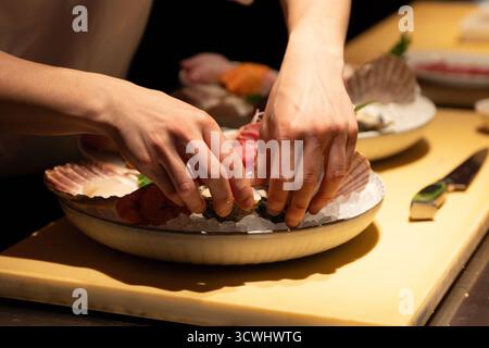 Lo chef esperto prepara sushi con ingredienti freschi su un piatto elegante, mostrando arte culinaria e attenzione ai dettagli. Foto Stock