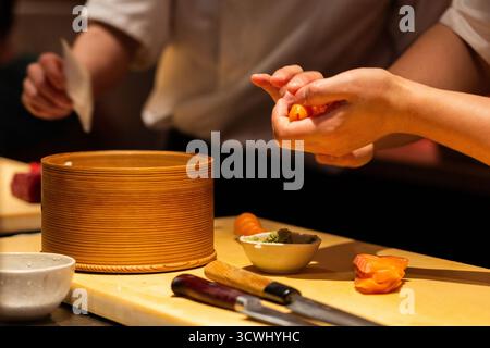 Lo chef esperto prepara sushi con ingredienti freschi, mostrando colori e consistenze vivaci, in un ambiente di cucina professionale. Foto Stock