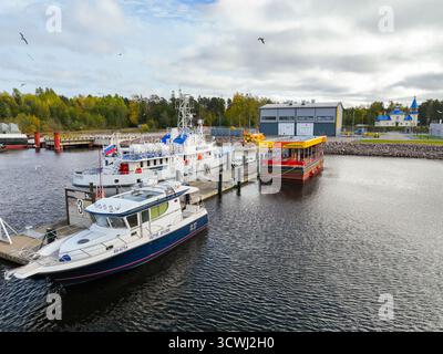 Vladimirovka, Russia - 13 maggio 2024: Vista di diverse barche e una stazione di servizio galleggiante rossa e gialla ormeggiata in un molo nel porto turistico, con edifici in Foto Stock