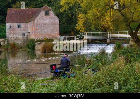 Sturminster Newton, Dorset, Regno Unito. 12 ottobre 2025. Meteo nel Regno Unito: Colori autunnali a Sturminster Newton Mill, Dorset. Sturminster Newton Mill è uno dei pochi mulini rimasti sul fiume Stour, parte di una serie di antichi mulini costruiti sul fiume. Si tratta di un mulino ad acqua completamente funzionante che produce farina, venduto nei negozi del Museo e del Mulino ed è un meraviglioso pezzo di archeologia industriale. Pescatore che pesca lungo le rive. Crediti: Carolyn Jenkins/Alamy Live News Foto Stock