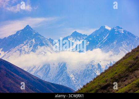 Le cime innevate si innalzano sopra le nuvole delle montagne Tian Shan. Foto Stock