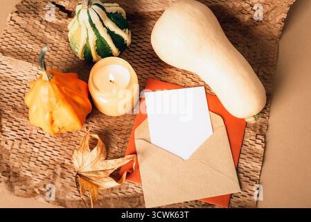 Busta con cartoncino vuoto, zucche, candela e foglia autunnale su sfondo in carta artigianale testurizzata. Il Ringraziamento, concetto di Halloween. Vista dall'alto, posizione piatta, mese Foto Stock