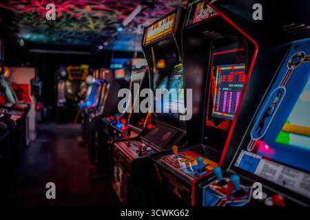 Le classiche macchine arcade verticali con schermi luminosi sono allineate all'interno di un ambiente di gioco retrò Foto Stock
