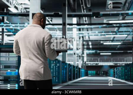 Programmatore nel data center che digita su notebook, scrive righe di codice, compila patch software per correggere i bug. Server hub professionale IT che utilizza script di programmazione su laptop, conducendo test su apparecchiature Foto Stock