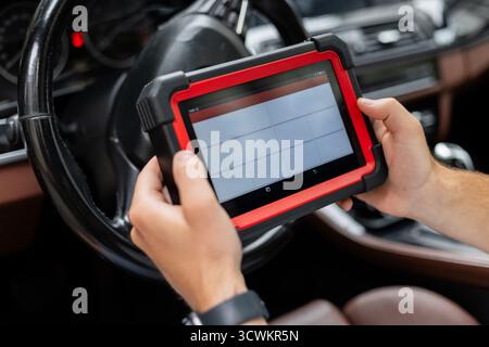 Tecnico del settore automobilistico che esegue la diagnostica del computer con il dispositivo palmare. Il meccanico tiene Un moderno scanner diagnostico all'interno Di Un'auto, controllando il veicolo Foto Stock