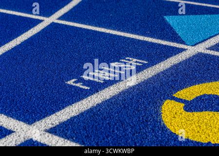 Foto ravvicinata di una pista da running blu all'aperto con linee bianche, con la parola, finitura, su una nuova pista. Foto Stock
