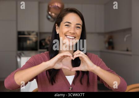 Positiva allegra donna latina degli anni '30 che unisce le dita a forma di cuore Foto Stock