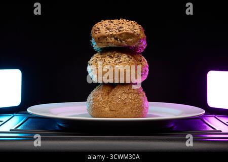 Quattro panini impilati uno sopra l'altro sotto l'illuminazione creativa al neon viola e ciano. Immagine concettuale del panificio per menu, poster o blog di cibo. Foto Stock