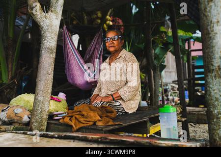 Balikpapan, Indonesia - 20 settembre 2025. Nonna anziana seduta con calma dopo aver messo suo nipote a dormire in un'amaca Foto Stock