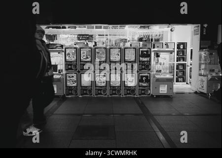 Una fila luminosa di macchine Gashapon e un gioco di artigli in una sala giochi di Osaka in bianco e nero Foto Stock