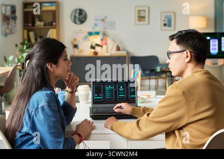 Uomo che spiega l'interfaccia dell'app mobile alla donna asiatica Foto Stock