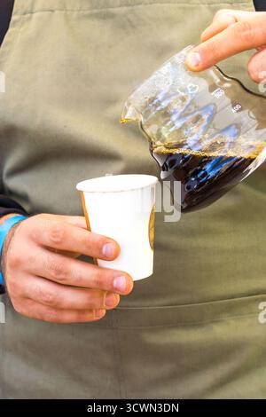 Un barista prepara il caffè utilizzando il metodo Pour-over versando acqua in un imbuto con filtro e chicchi di caffè durante una festa del caffè. Foto Stock