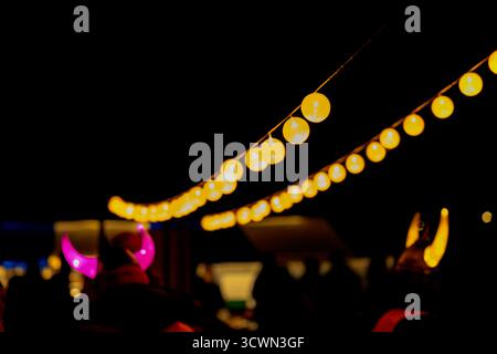 Due fili di calde luci gialle a spirale illuminano il cielo notturno, creando un'atmosfera festosa e invitante. Sagome di persone sotto, Foto Stock