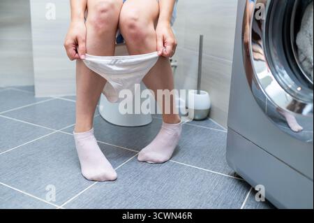 Donna seduta sul bagno, di fronte problemi urinari o intestinali, concetto di problema di salute, disturbi digestivi o urinari, scena del bagno Foto Stock