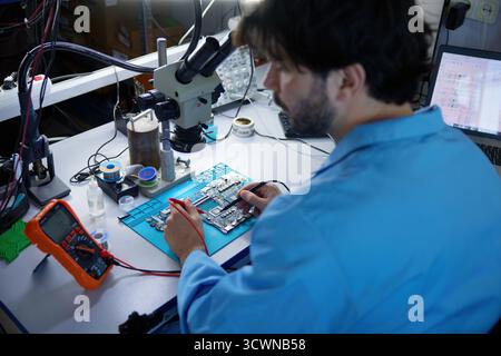 Il tecnico si è impegnato attivamente in lavori critici sulla scheda a circuiti stampati osservando al microscopio Foto Stock
