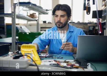 Un uomo che lavora con un cappotto blu si concentra sul lavoro con una scheda madre Foto Stock