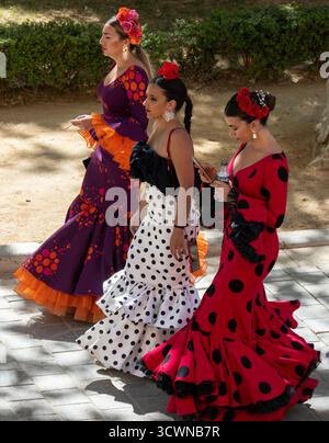 Siviglia, Spagna - 23 aprile: Tre donne in abiti flamenco colorati che camminano insieme all'aperto Foto Stock