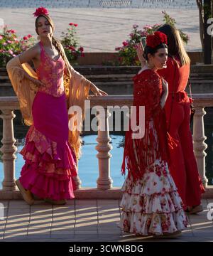 Siviglia, Spagna - 23 apr 23: Tre donne in abiti flamenco tradizionali con una caratteristica acquatica, colori vivaci, motivi floreali e scialli decorativi, sh Foto Stock