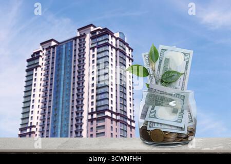 Barattolo con dollari e monete contro il condominio. Risparmiare denaro per comprare un appartamento Foto Stock