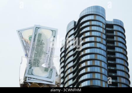 Barattolo con dollari e monete contro il condominio. Risparmiare denaro per comprare un appartamento Foto Stock