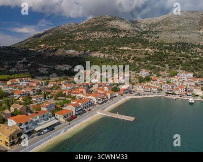 Vista aerea degli edifici baciati dal sole con tetti in terracotta che contrastano con le acque azzurre del porto, abbracciati dall'aspro sfondo delle montagne, Agia Effimia, Cefalonia, Grecia. Foto Stock