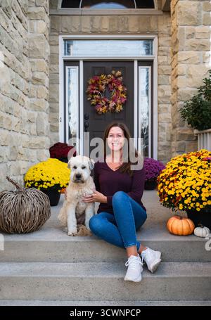Donna e cane seduti sul gradino anteriore di casa decorati per l'autunno. Foto Stock