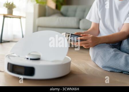 Aspirapolvere robotizzato bianco su pavimento in legno. Tecnologia di pulizia intelligente Foto Stock
