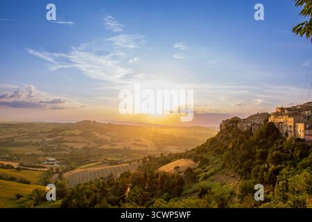 Il tramonto dorato inonda Sant'Elpidio a Mare di luce calda, con sagome di colline lontane che incorniciano il tranquillo paesaggio urbano. Un mix sereno di architettura Foto Stock