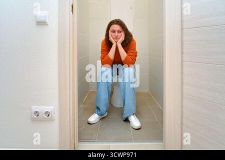 Donna seduta in bagno con espressione triste e stanca. Concetto di depressione, problema di salute, o pensare nello spazio della privacy. Foto Stock