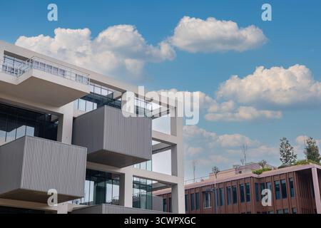Edificio moderno e minimalista con facciata in vetro e balconi in cemento, adagiato contro il cielo blu con nuvole. Edificio per uffici con design di bellezza Foto Stock
