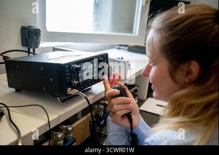 Giovane donna che utilizza un ricetrasmettitore radio amatoriale VHF/UHF, tiene in mano il microfono e rappresenta donne e YLS nei moderni campi DI comunicazione e STEM. Foto Stock