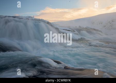 Vista delle potenti cascate che corrono su rocce ghiacciate sotto un cielo pastello, creando un affascinante mix di potenza grezza e bellezza serena, Gullfoss, Hrunamannahreppur, Islanda. Foto Stock