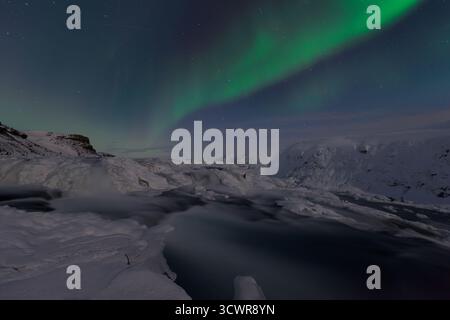 Vista dell'eterea danza verde dell'aurora boreale sopra la cascata ghiacciata e il paesaggio innevato, un balletto celeste nell'aria notturna frizzante, Gullfoss, Hrunamannahreppur, Islanda. Foto Stock