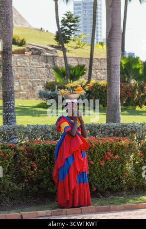 Cartagena, Colombia - 16 dicembre 2023: Ritratto iconico di una Palenquera, un simbolo culturale di Cartagena, in un giardino tropicale con la città Foto Stock