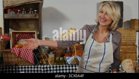 fornaio sorridente in grembiule che presenta cestini di pane e vasetti sul tavolo al banco, spazio copia Foto Stock