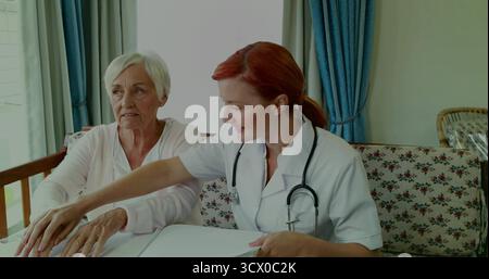 Puntare l'operatore sanitario che guida il paziente sul divano floreale che esamina documenti, con stetoscopio Foto Stock