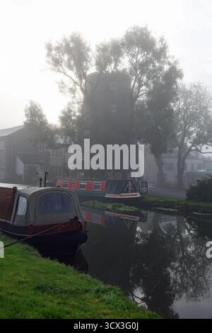 La nebbia autunnale di prima mattina nasconde il mulino a vento e le barche a remi sul canale Leeds e Liverpool nel villaggio di Parbold nel Lancashire occidentale. Foto Stock