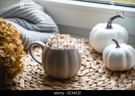 Cioccolata calda o caffè autunnale con marshmallow, zucche e candela sul davanzale della finestra. Condire le bevande. Primo piano. Foto Stock