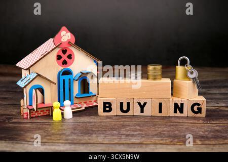 "Modello di casa in miniatura con monete, lucchetto e chiavi accanto a blocchi di legno che indicano "ACQUISTO", simboleggiano l'acquisto di beni immobili, investimenti immobiliari, e. Foto Stock