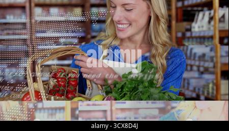 Donna sorridente che indossa un grembiule che prepara pomodori e verdure a foglia verde nel cestino di vimini nella corsia del supermercato Foto Stock