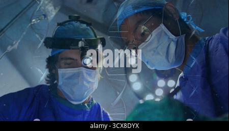 Chirurghi in funzione che indossano scrub e maschere sotto le luci a padiglione con fari in sala operatoria Foto Stock