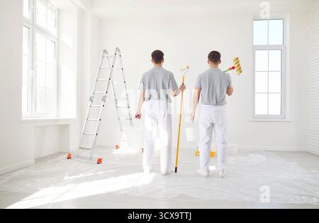 Due pittori professionisti in abiti leggeri che dipingono una parete bianca. Concetto di riparazione. Foto Stock