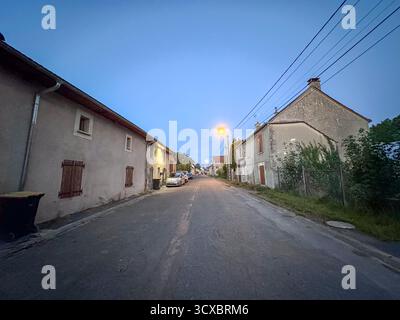Bergnicourt, Rethel, Ardenne, Grand-Est, Francia, 28 agosto 2025, Una tranquilla strada del villaggio al crepuscolo, delicatamente illuminata da lampioni, catturando l'essenza del tranquillo fascino rurale Foto Stock