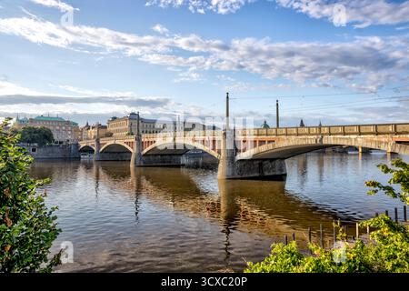 Ponte della Legione che attraversa il fiume Moldava a Praga, Repubblica Ceca, con linee di tram e architettura della città riflessa nelle acque calme sottostanti Foto Stock
