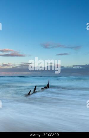 I resti arrugginiti della nave a vapore Maheno sono visibili nell'acqua, parzialmente sommersi. Il relitto è sulla costa, circondato dalle onde. Foto Stock
