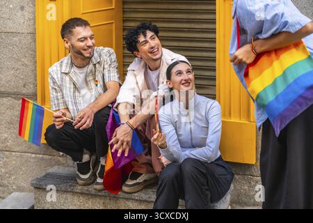 Gruppo di amici diversi che esprimono gioia e appartenenza, tenendo bandiere arcobaleno e portando con sé una borsa arcobaleno, celebrando l'orgoglio gay e lgbtqia e inclusioni Foto Stock