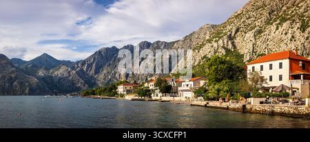 Vista panoramica di Dobrota, Montenegro, con tradizionali case mediterranee, torre della chiesa e montagne Foto Stock