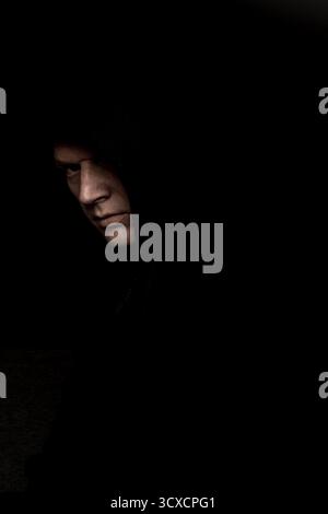uomo spaventoso con felpa con cappuccio nera che sembra sinistro, oscuro e inquietante ritratto Foto Stock