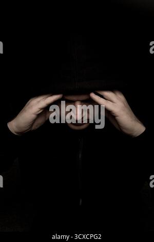 uomo spaventoso con felpa con cappuccio nera che sembra sinistro, oscuro e inquietante ritratto Foto Stock
