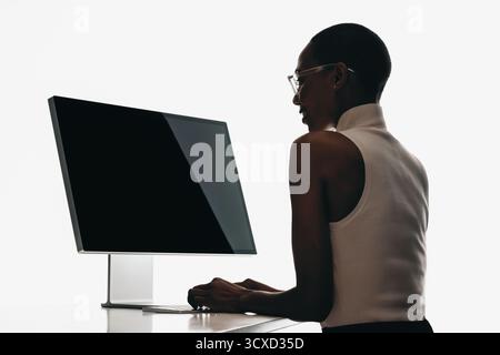 Elegante professionista che utilizza un computer desktop in ufficio, mostrando concentrazione e produttività. Perfetto per temi di lavoro o spa Foto Stock